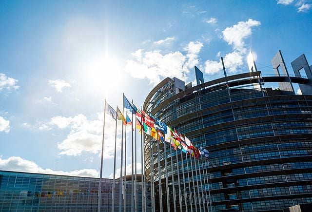 Wide angle view of large facade European PArliament building in Strasbourg with all EU member Flags including United Kingdom - clear blue sky and scattered clouds
