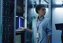 Portrait of African American woman working as IT engineer and standing among server racks in data center room